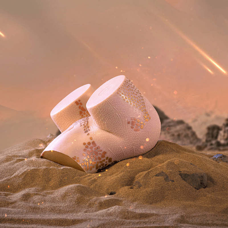 Realistic male masturbator with textured pink skin and gold speckles, nestled in desert sand under warm glow
