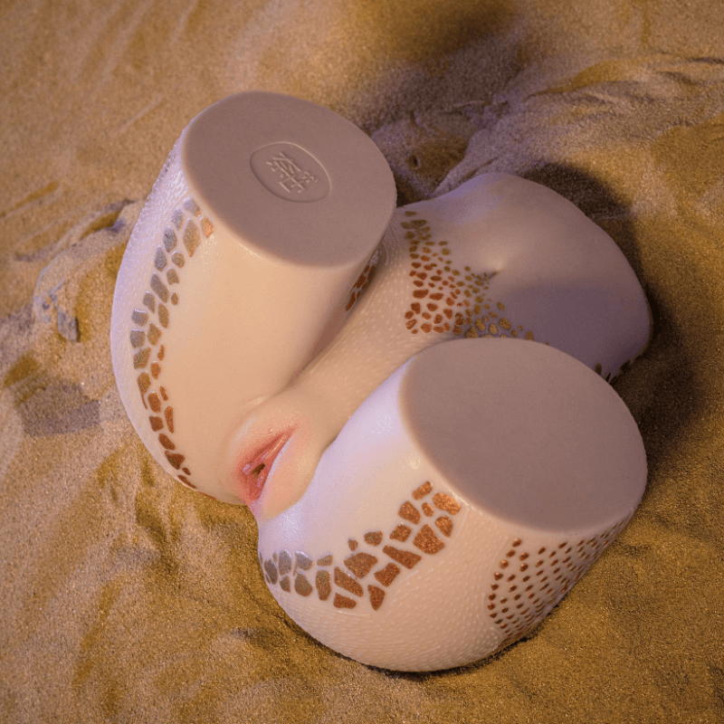 Realistic male masturbator with textured skin, gold mosaic patterns, and lifelike lips on sandy surface