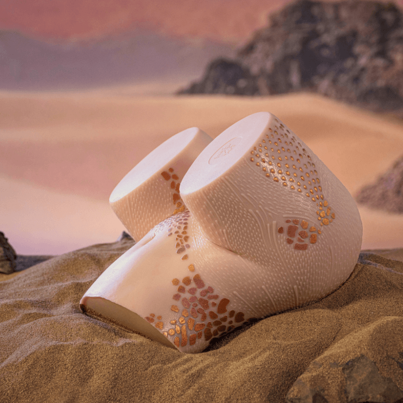 Realistic male masturbator with textured skin, gold speckles, and dual openings, set in desert sand