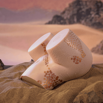 Realistic male masturbator with textured skin, gold speckles, and dual openings, set in desert sand