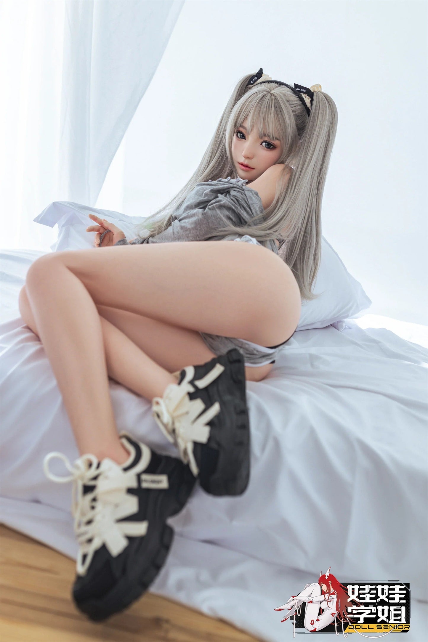 Realistic female doll with silver pigtails, gray top, black sneakers, lounging on white bed
