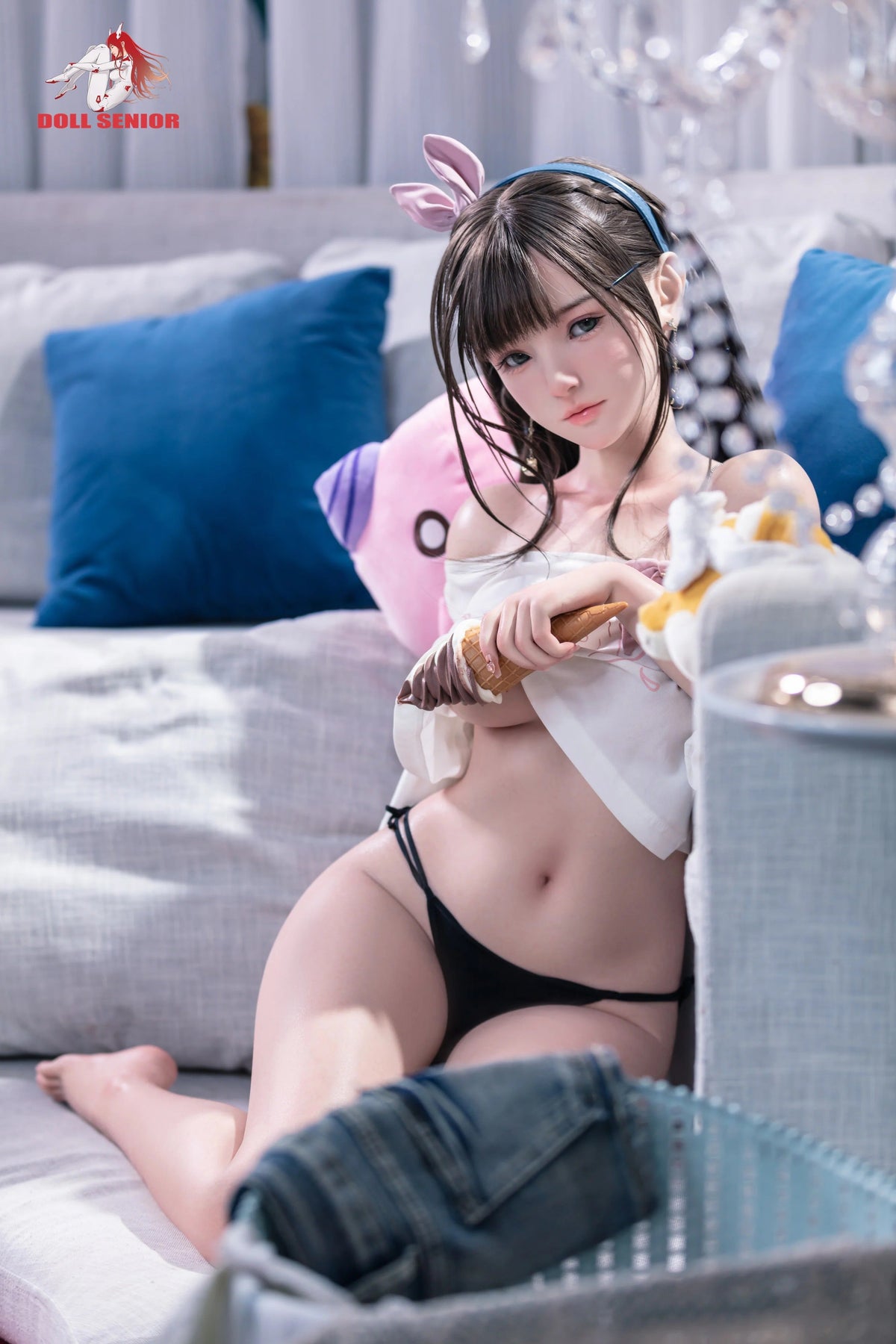 Realistic female doll with brown hair, pink bunny ears, holding ice cream, wearing black lingerie on gray couch