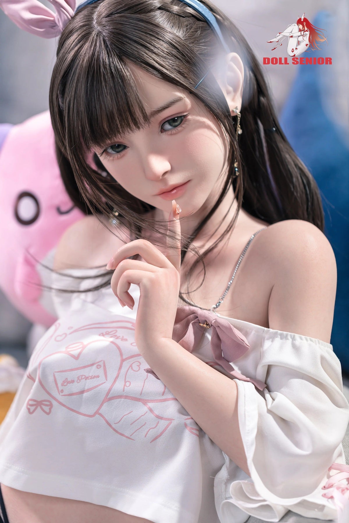 Realistic female doll with brown hair, green eyes, wearing white top with pink bow and bunny ears