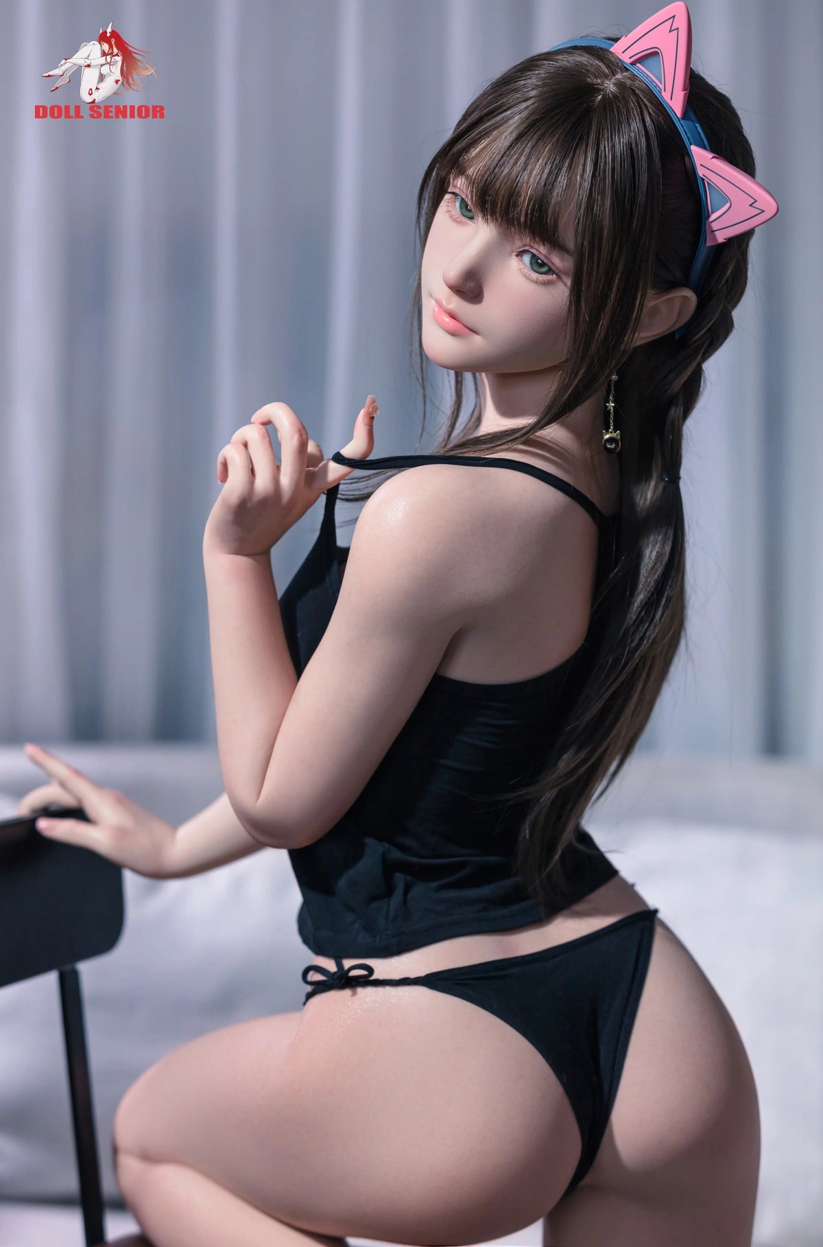 Realistic female doll with brown hair, green eyes, wearing black lingerie and pink cat ears, seated on a chair.