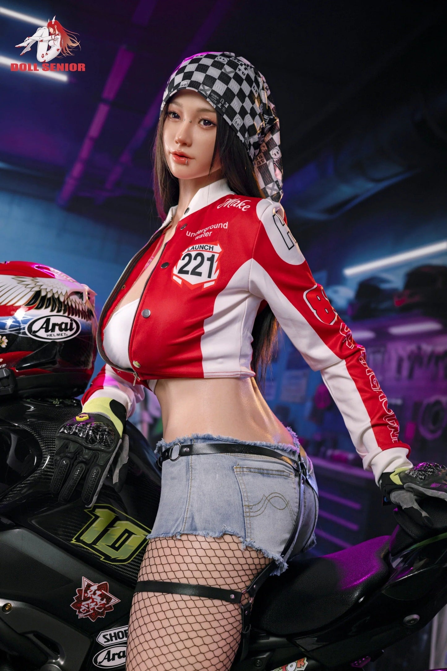 Realistic female doll in red racing jacket, denim shorts, fishnet stockings, posed on motorcycle with checkered hood and Arai helmet nearby