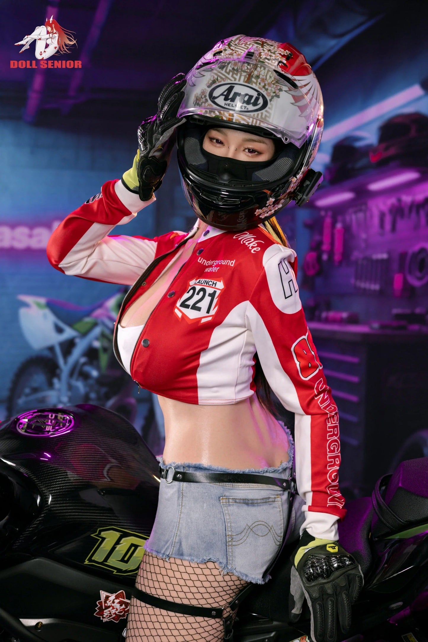 Realistic female doll in red racing jacket, floral helmet, and denim shorts posing beside motorcycle