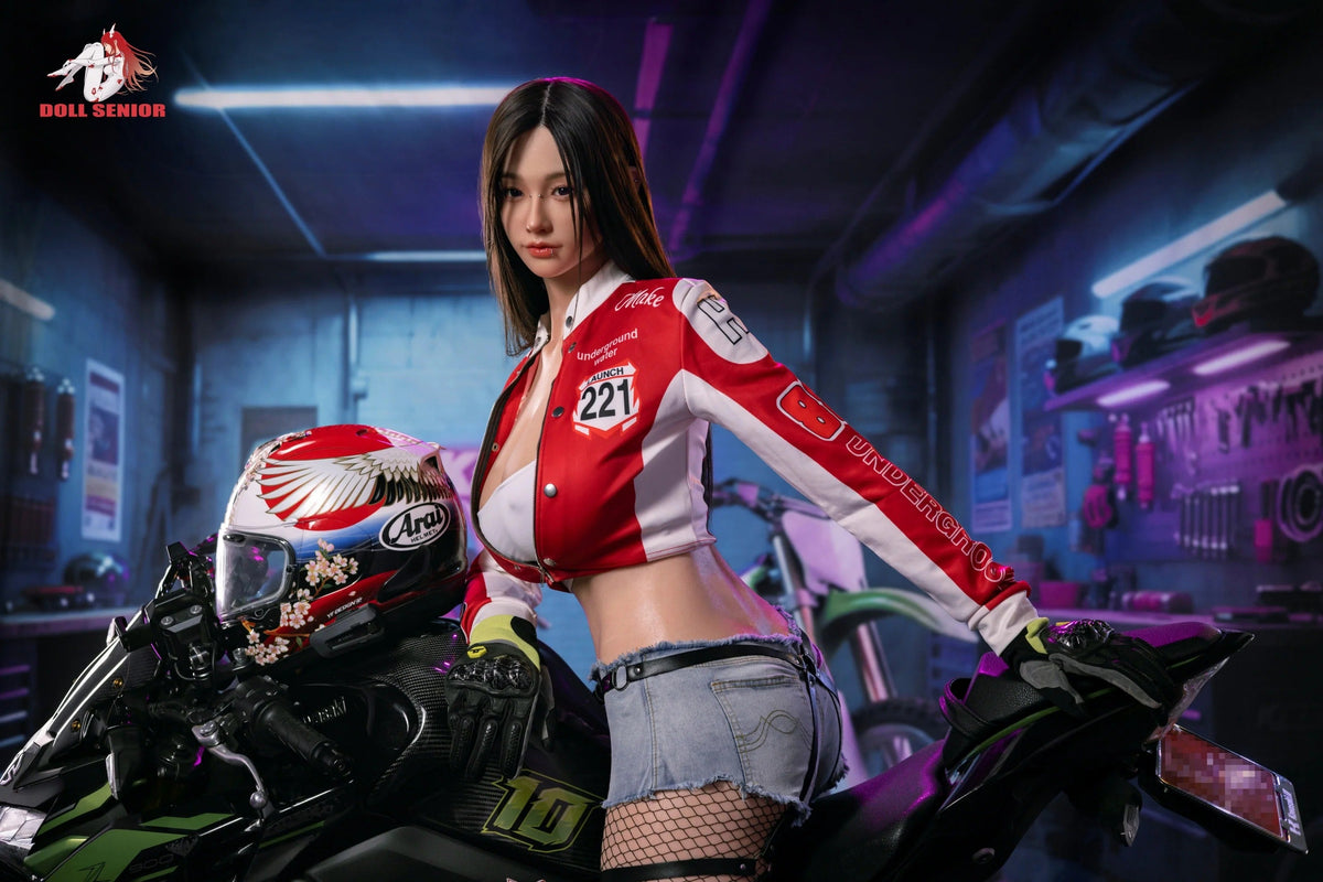 Realistic female doll in red racing jacket and denim shorts, posed on motorcycle in garage setting