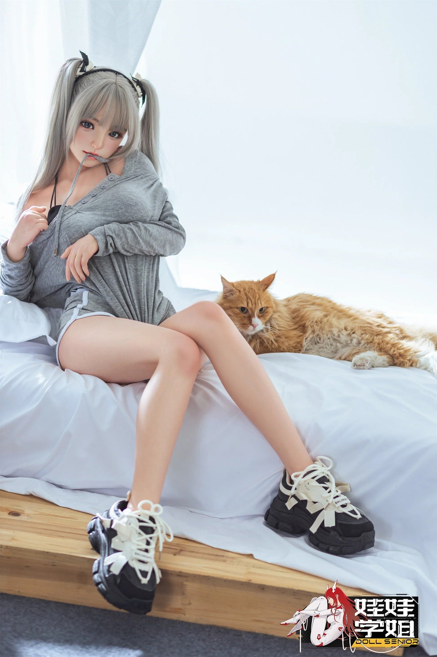 Realistic anime-style doll with silver pigtails, grey hoodie, and black sneakers, sitting beside a fluffy orange cat on a bed.
