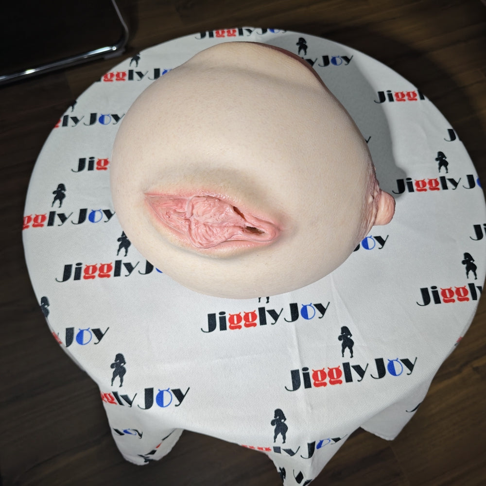 Realistic flesh-toned male masturbator with detailed vaginal opening, resting on branded fabric