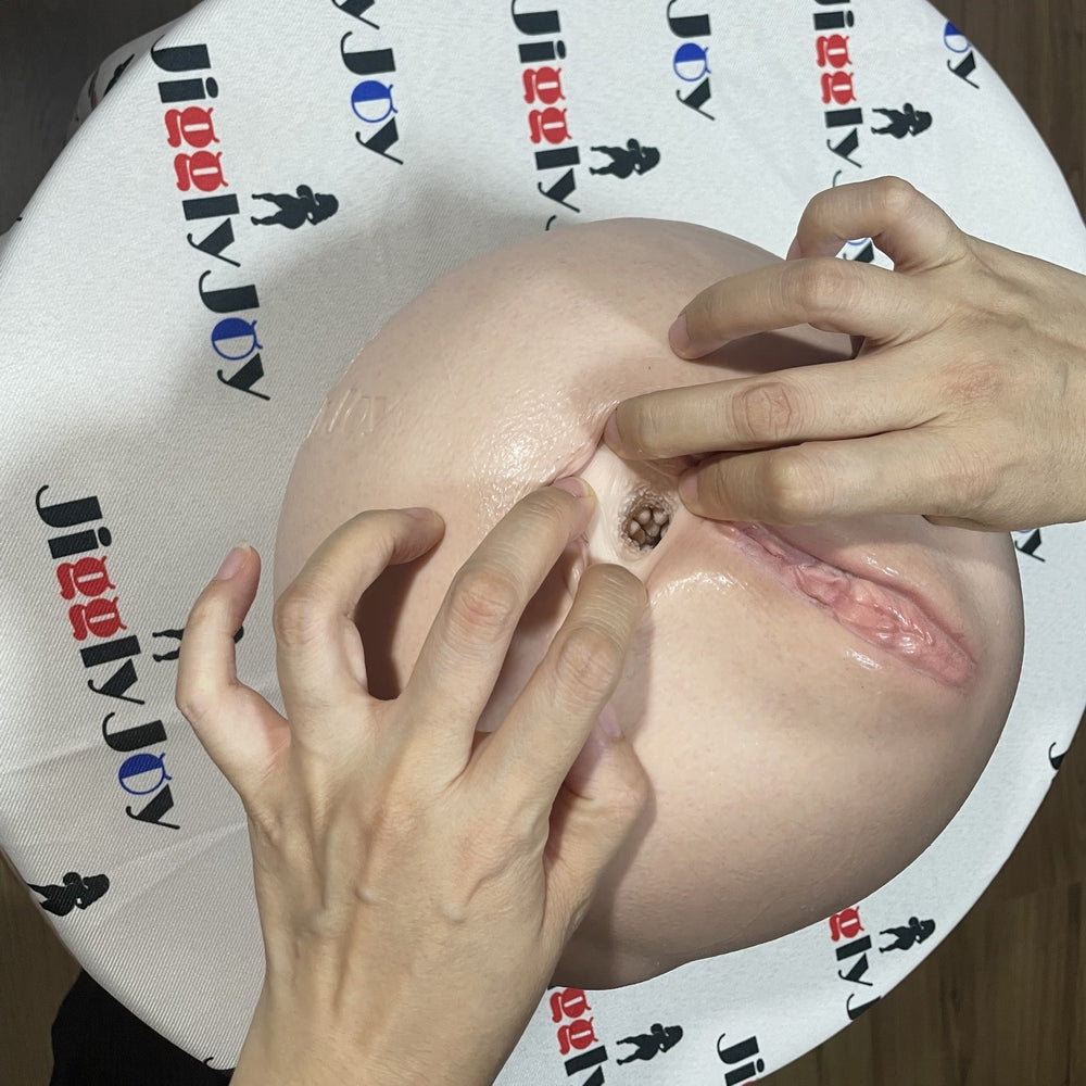 Realistic flesh-toned male masturbator with detailed vaginal and anal openings, soft silicone texture, held by hands on branded mat