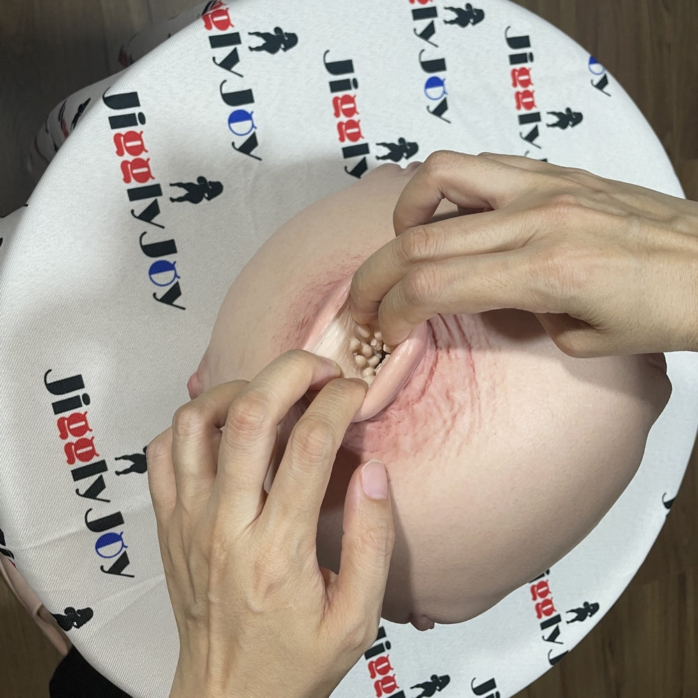 Realistic male masturbator with textured interior and lifelike skin tone, shown with hands demonstrating use on branded surface