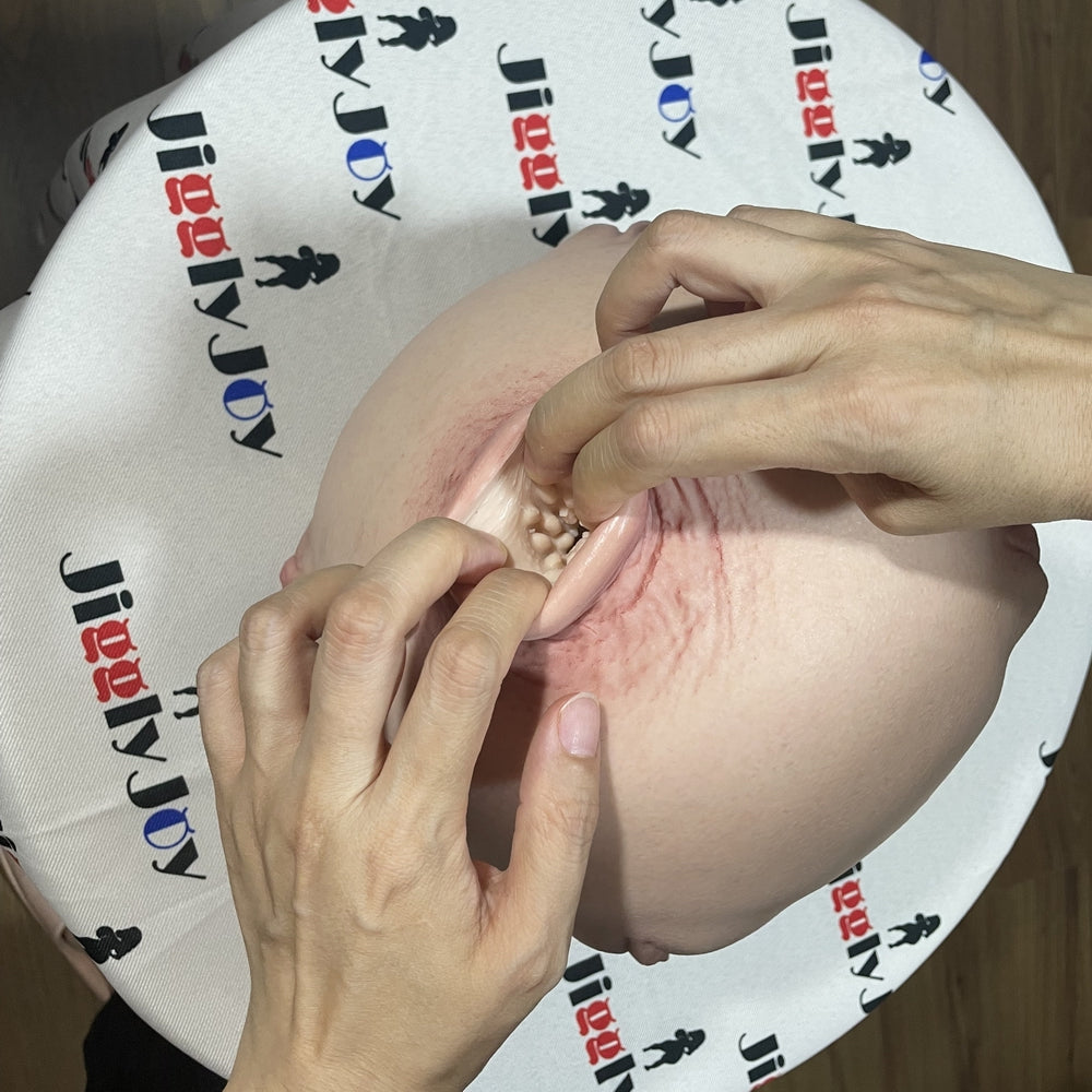 Realistic silicone male masturbator with textured interior and natural skin tone, shown with hands demonstrating use on branded surface