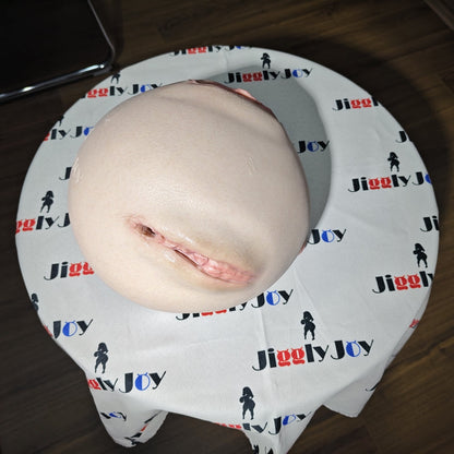 Realistic flesh-toned male masturbator with detailed vaginal opening, resting on branded cloth