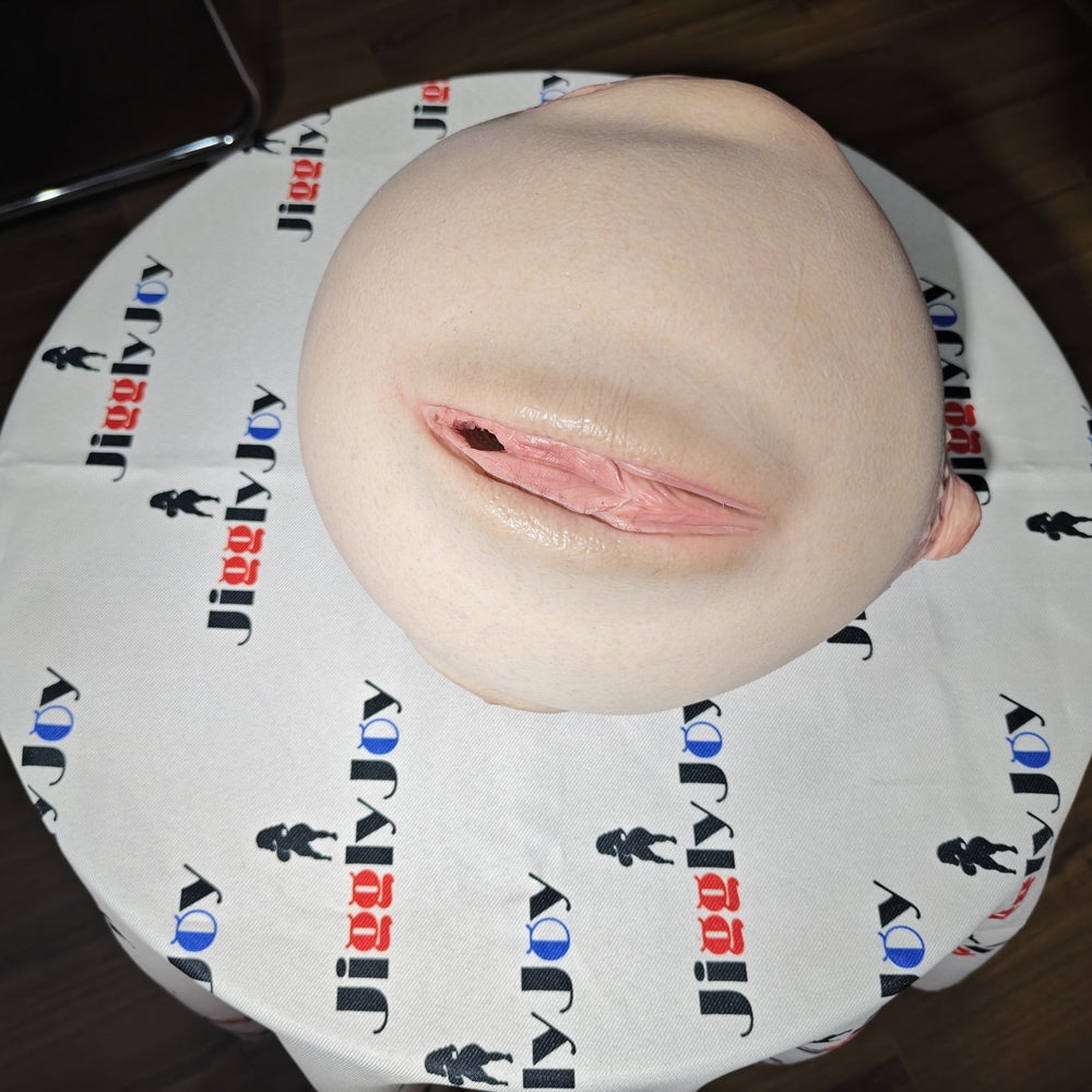 Realistic flesh-toned male masturbator with detailed labia and vaginal opening, resting on branded fabric